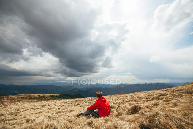 Молодий чоловік сидить у полі з бурхливим небом на фоні — стокове фото
