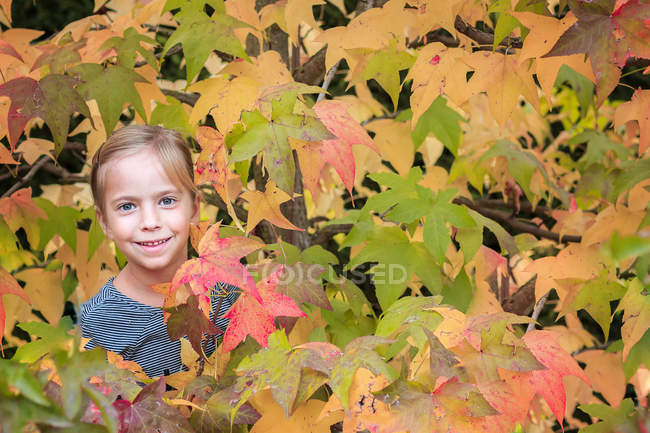 Sonriente chica de pie entre las hojas de otoño - foto de stock