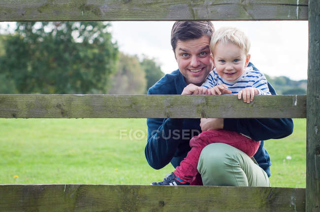 Улыбающийся отец с сыном, смотрящим через забор в парке — стоковое фото