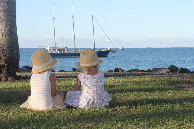 Two cute little sisters in straw hats sitting and looking at ship — Stock Photo