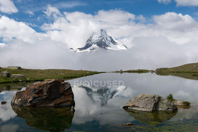 Switzerland, Valais, Zermatt, Rocks in still waters of Stellisee lake and Matterhorn mountain in clouds — Stock Photo