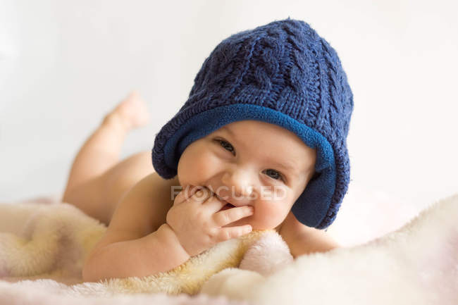 Portrait de bébé garçon portant un chapeau en tricot bleu couché sur une couverture — Photo de stock