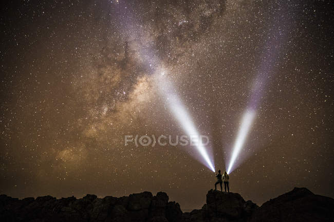 Silhuetas de duas pessoas com tochas sob céu estrelado — Fotografia de Stock