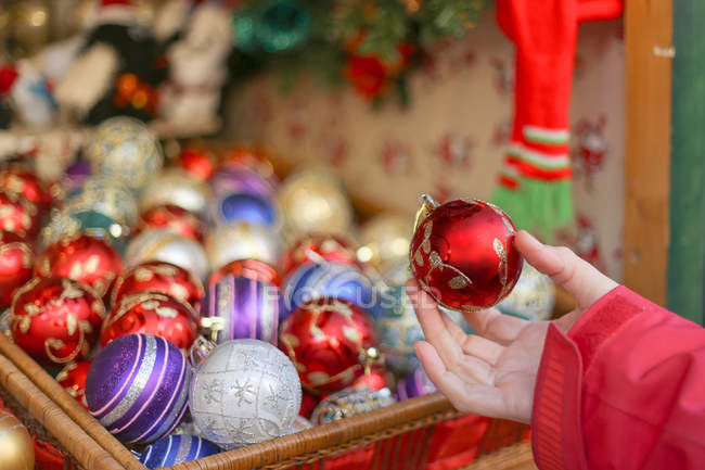 Cropped image of Hand holding red Christmas bauble with other baubles in background — Stock Photo