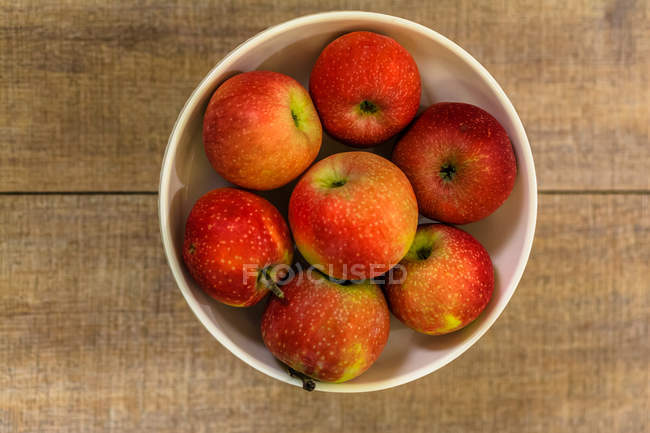 Apples in white fruit bowl over wooden table — Stock Photo