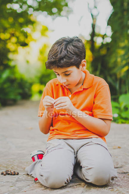 Retrato de menino sentado no beco do parque, olhando para sementes de plantas — Fotografia de Stock