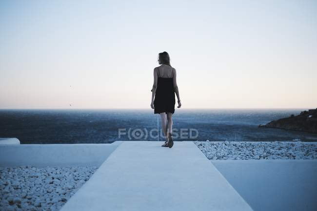 Вид сзади на женщину, идущую по пристани и смотрящую на море — стоковое фото
