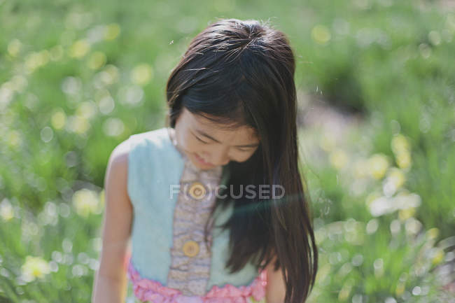 Menina olhando para baixo, enquanto em pé no prado verde — Fotografia de Stock