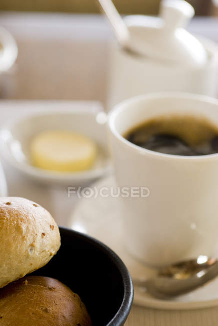 Rolos de pão com manteiga e café preto na mesa — Fotografia de Stock