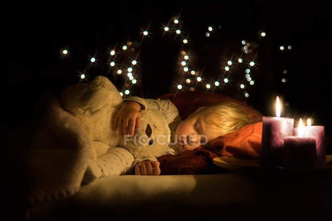 Хлопчик спить з плюшевим і теплим свічковим світлом — стокове фото