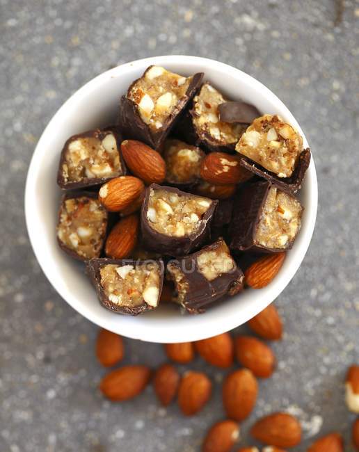 Chocolate candy bars cut into pieces mixed with whole almonds in white porcelain bowl — Stock Photo