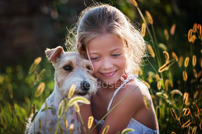 Retrato de niña sonriente abrazando al perro en el campo - foto de stock