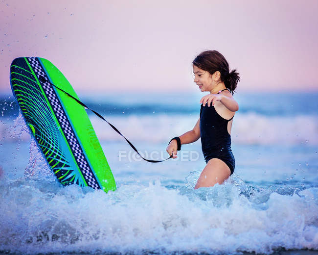 Sorrindo Menina com prancha de surf jogando na água — Fotografia de Stock