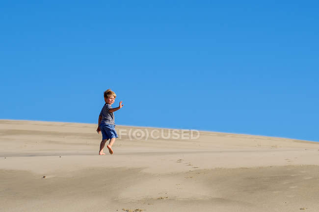 Мальчик бежит по песчаному пляжу на фоне голубого неба — стоковое фото
