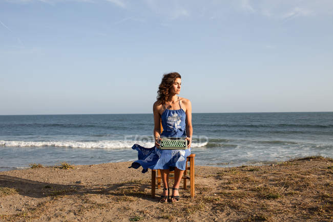 Mujer sentada en silla en la playa con máquina de escribir - foto de stock