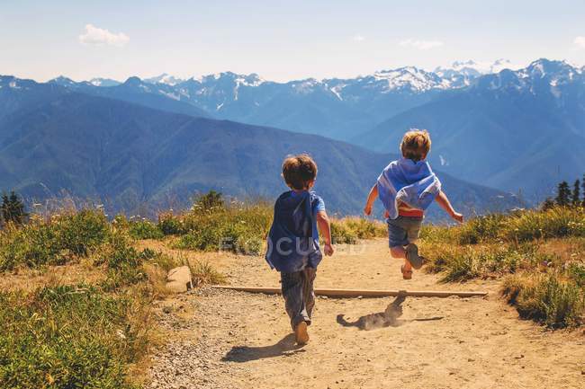 Rear view of boys running on path through mountains — Stock Photo