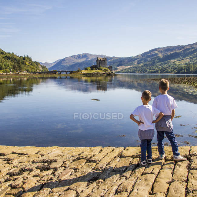 Rear view of boys looking at Eileen Donan Castle, UK, Scotland — Stock Photo