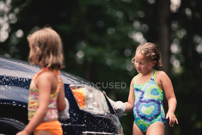 Two cute sisters washing car outdoors — Stock Photo