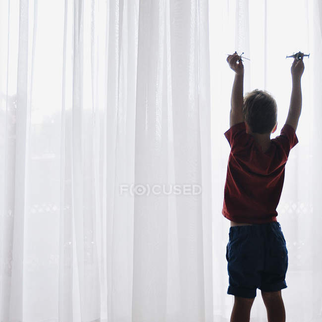 Menino brincando com aviões brinquedos ao lado da janela — Fotografia de Stock