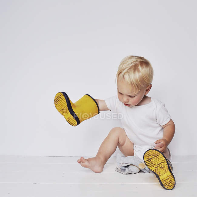 Мальчик играет с желтыми сапогами Веллингтона на белом фоне — стоковое фото