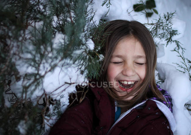 Chica con los ojos cerrados de pie en las ramas de los árboles nevados - foto de stock