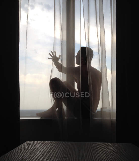 Mann sitzt mit ausgestrecktem Arm auf Fensterbank und blickt auf Aussicht — Stockfoto