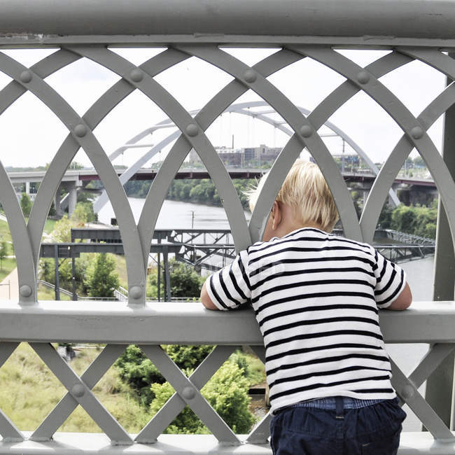 Menino olhando através de grades na ponte — Fotografia de Stock