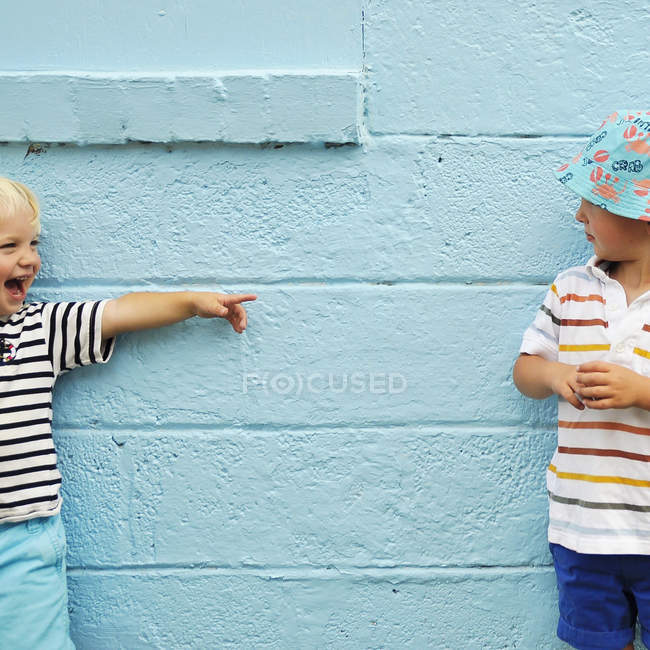 Zwei kaukasische Jungen, die neben der Mauer stehen, einer zeigt auf den anderen — Stockfoto