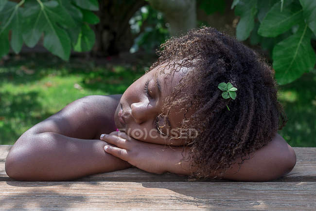 Маленькая девочка дремлет с головой на руках на столе — стоковое фото
