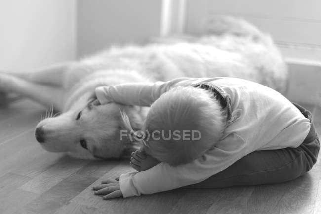 Маленька дівчинка погладжує собаку на підлозі, монохромний — стокове фото