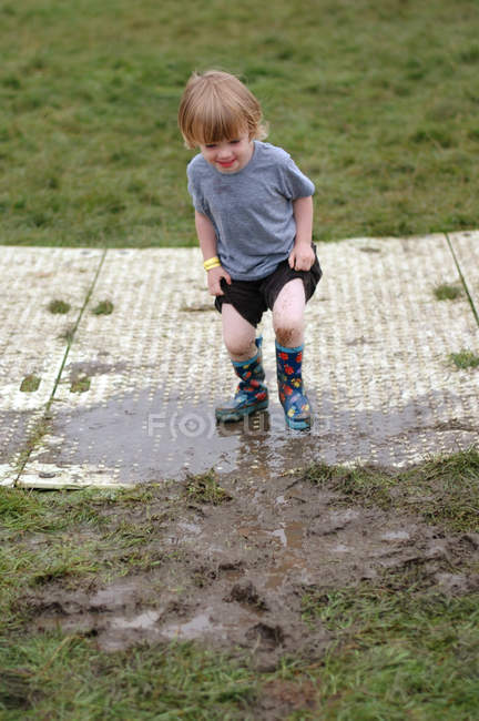 Menino usando botas de borracha se divertindo na lama — Fotografia de Stock