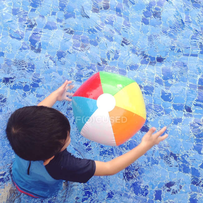 Menino brincando com bola de praia colorida na piscina — Fotografia de Stock