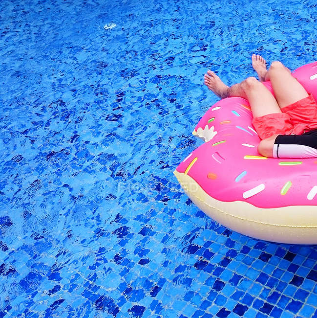 Abgeschnittenes Bild eines Mannes, der sich auf aufblasbarem Donut in einem Swimmingpool entspannt — Stockfoto
