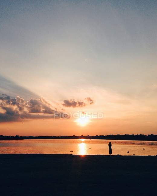 Hermoso cielo puesta de sol y silueta de mujer en la playa en el agua de mar - foto de stock