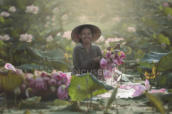 Donna contadina sorridente mantiene fiore di loto sul lago mattina a Sakon Nakhon, Thailandia — Foto stock