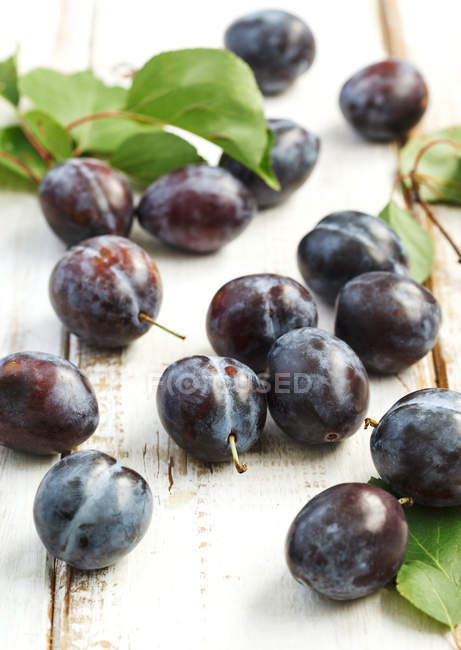 Fresh plums with leaves on wooden background. — Stock Photo