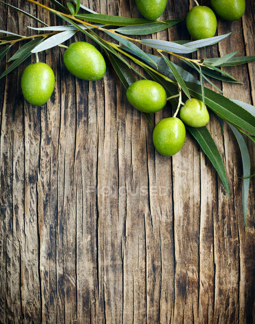Frische grüne Oliven mit Blättern auf Holzgrund — Stockfoto