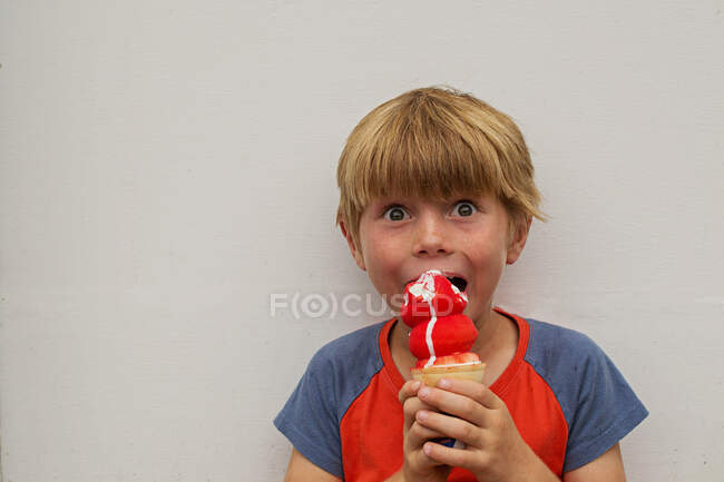 Хлопчик їсть морозиво на білому тлі стіни — стокове фото