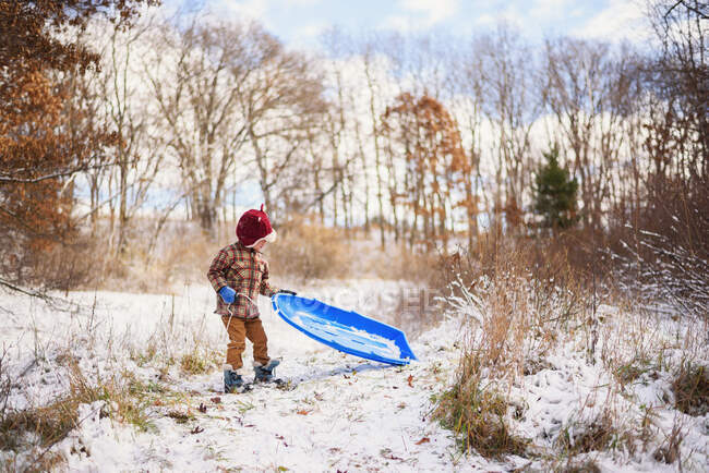 Мальчик, стоящий в снегу с санями на природе — стоковое фото