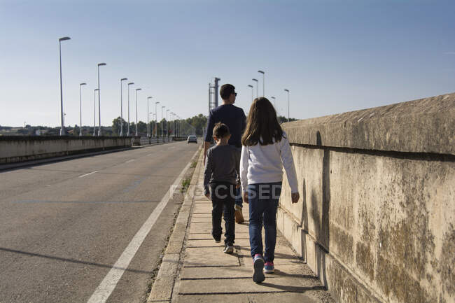 Padre y dos niños caminando por la calle - foto de stock
