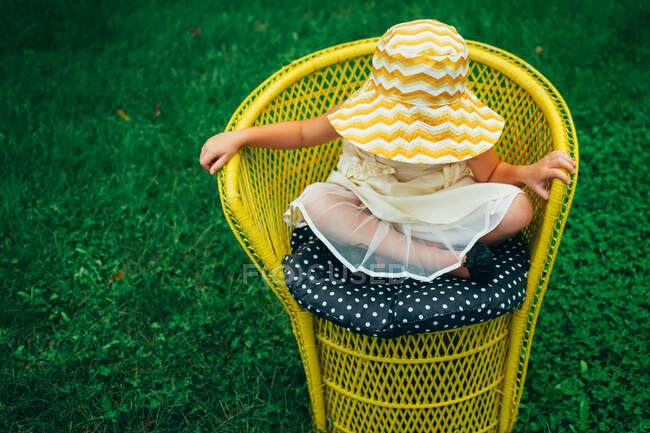 Дівчина в літньому капелюсі сидить в садовому кріслі — стокове фото