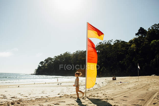 Mädchen am Strand läuft an Lebensretter-Flaggen vorbei — Stockfoto