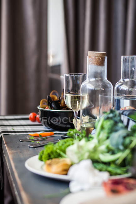 Mejillones, verduras, vino y agua en la mesa - foto de stock