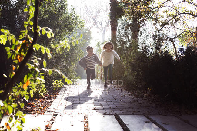 Мальчик и девочка бегут по парку, держась за руки — стоковое фото