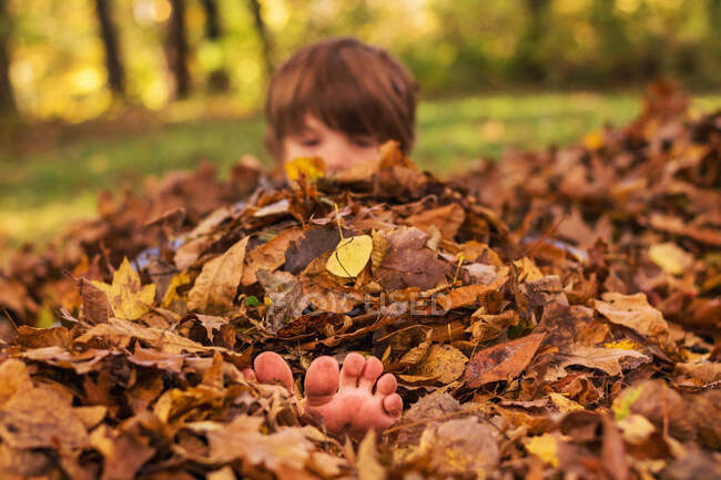 Niño enterrado en un montón de hojas de otoño - foto de stock