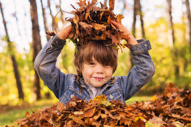 Junge spielt in einem Haufen Herbstlaub — Stockfoto