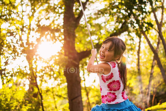 Chica riendo sentada en un columpio de cuerda - foto de stock