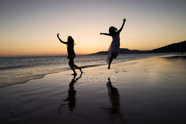 Силуэт двух женщин, танцующих на пляже лос Лансес на закате, Фафа, Кадис, Андалусия, Испания — стоковое фото