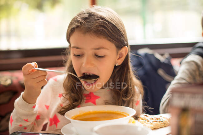 Menina comendo sopa enquanto olha para seu telefone celular — Fotografia de Stock