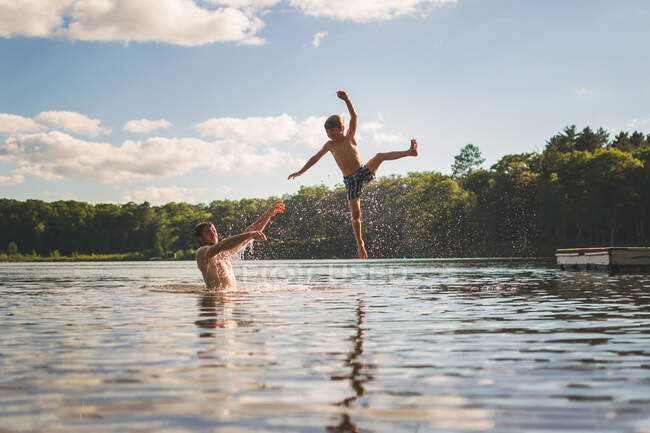 Padre lanzando hijo en el aire en un lago - foto de stock